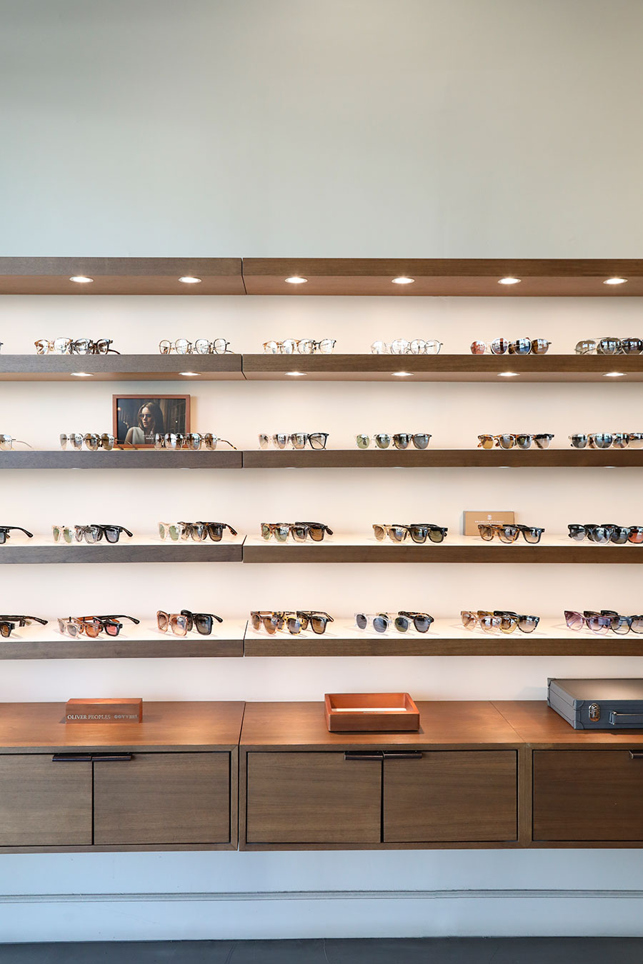Oliver-Peoples A collection of glasses on elegant wooden shelves in a store